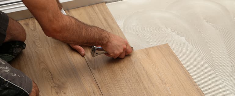 mãos aplicando piso sobre piso de madeira | Blog Agência FG