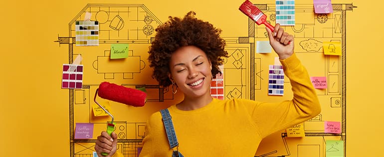 Mulher segurando pinceis de pintura em um fundo amarelo |  como reformar a casa gastando pouco