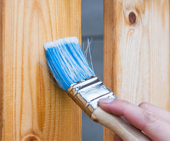 Pincel com tinta azul aplicado em madeira para proteção e acabamento, destacando a importância da tinta para madeira em trabalhos de pintura e reforma.