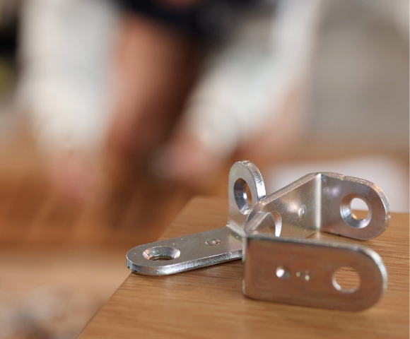 Dobradiça com amortecedor: Detalhe de uma dobradiça metálica com amortecimento, fixada em uma base de madeira, com parafusos e peças de fixação visíveis para instalação.